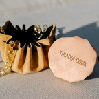 Natural cork Porto jewelry pouch shown open on a pink branded display base, with its drawstring and cork flower details visible; display props are not included.